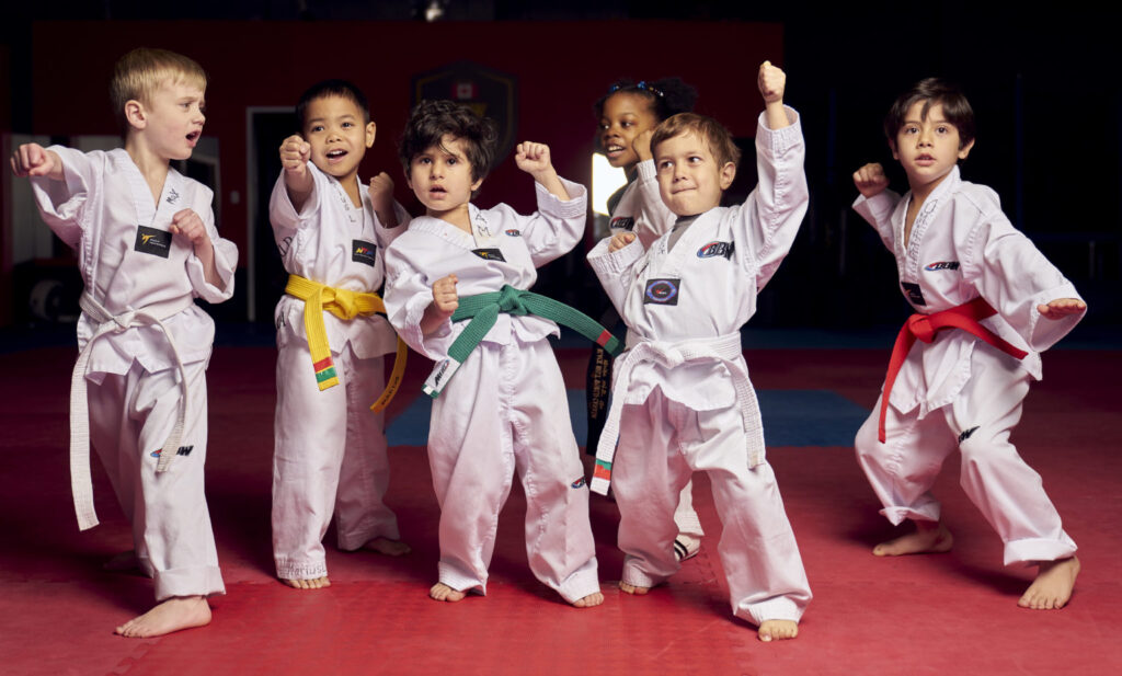 A diverse group of junior martial arts students in white uniforms performing a powerful kihap shout during their martial arts for kids session to build self confidence.
