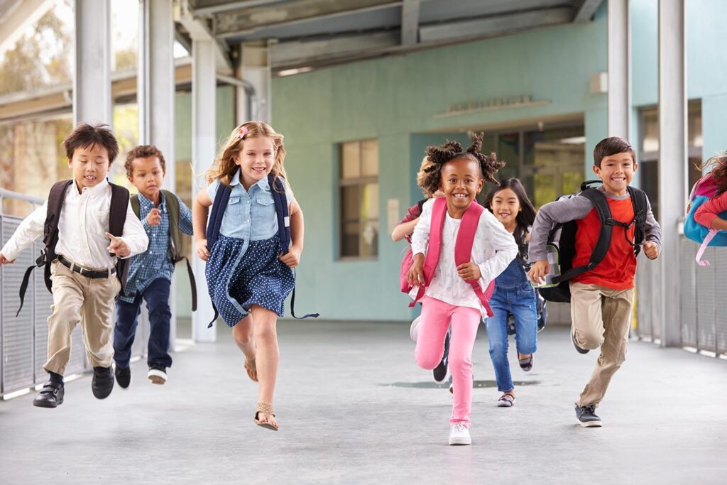 A group of diverse children running happily through a hallway during an active youth program focused on physical fitness.