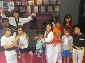 A group of diverse students smiling and posing in a local taekwondo school to showcase positive peer relationships.