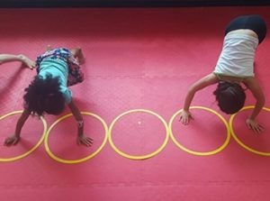 Young students practicing coordination exercises on a red mat during a youth fitness class to improve gross motor skills.