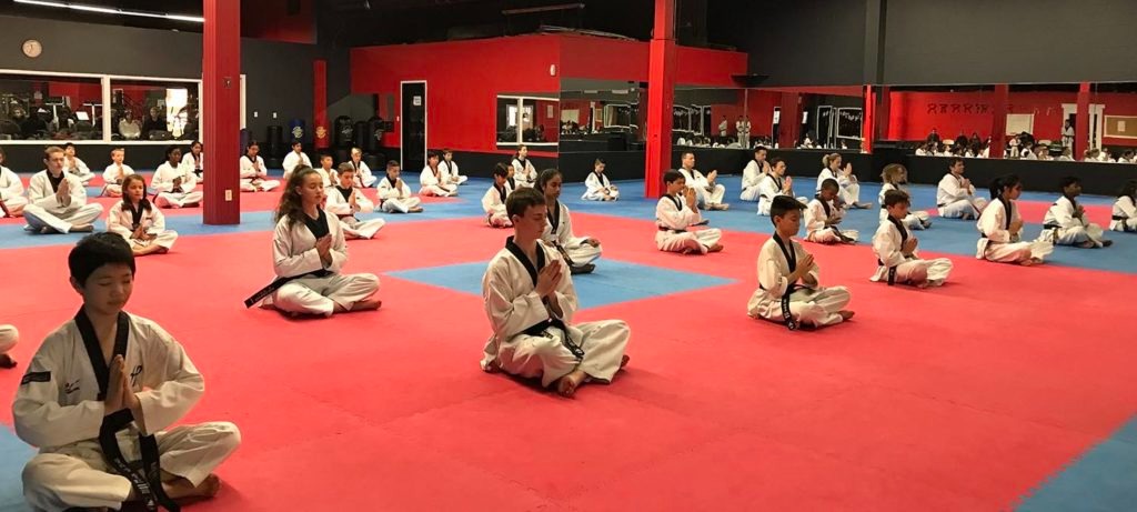 A large group of students in a professional martial arts dojang practicing seated meditation to improve mental focus and discipline.