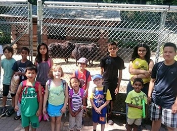 A group of happy students posing in front of a zoo exhibit during a martial arts summer program to encourage outdoor learning.