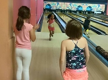 Young girls cheering at a bowling alley during a summer camp activity designed to improve childhood social skills.