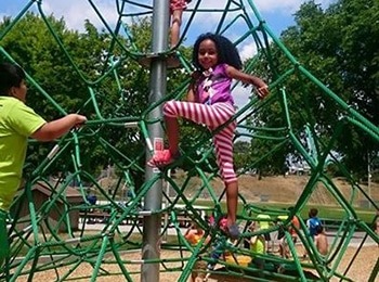 A young girl smiling while climbing a rope structure during a martial arts camp to improve childhood physical health.
