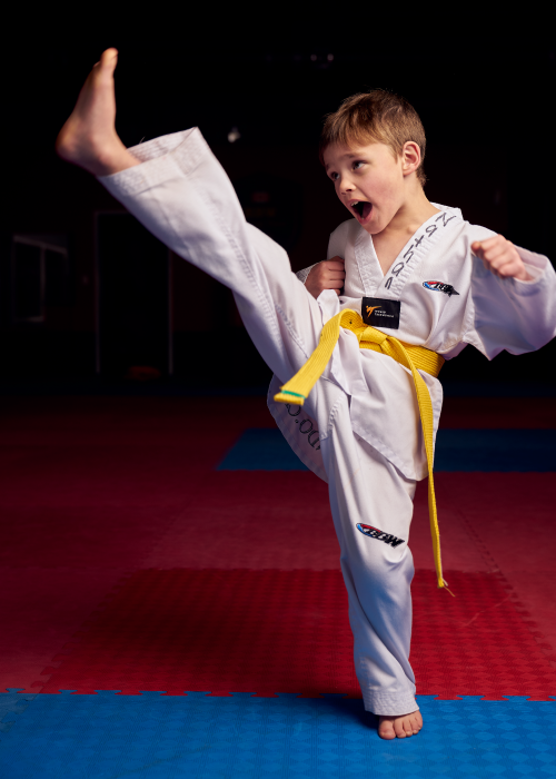 A young yellow belt student demonstrating focus and power while executing a high front kick during a junior martial arts session.